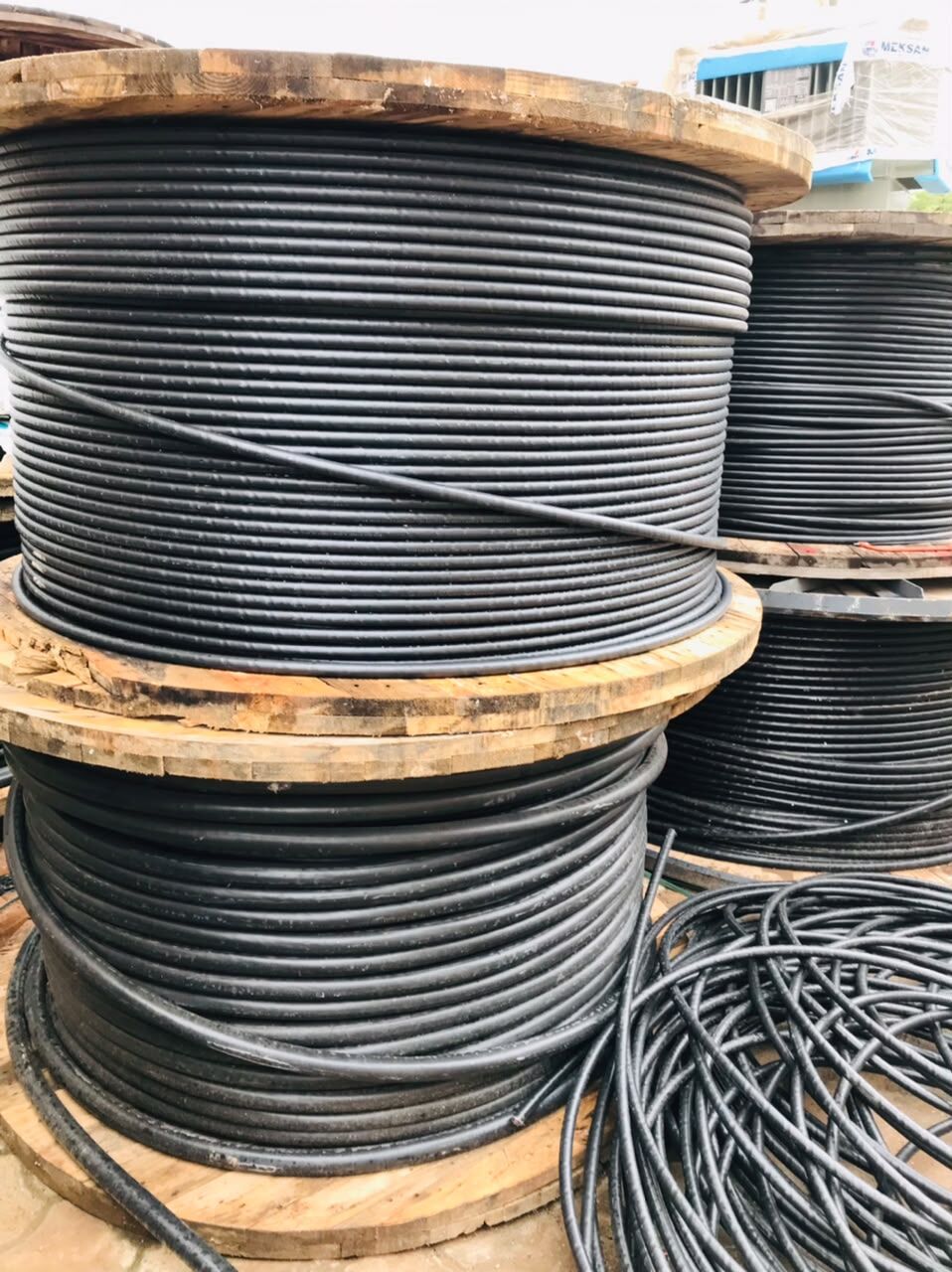 Wooden drums of black armoured cable stacked in a yard