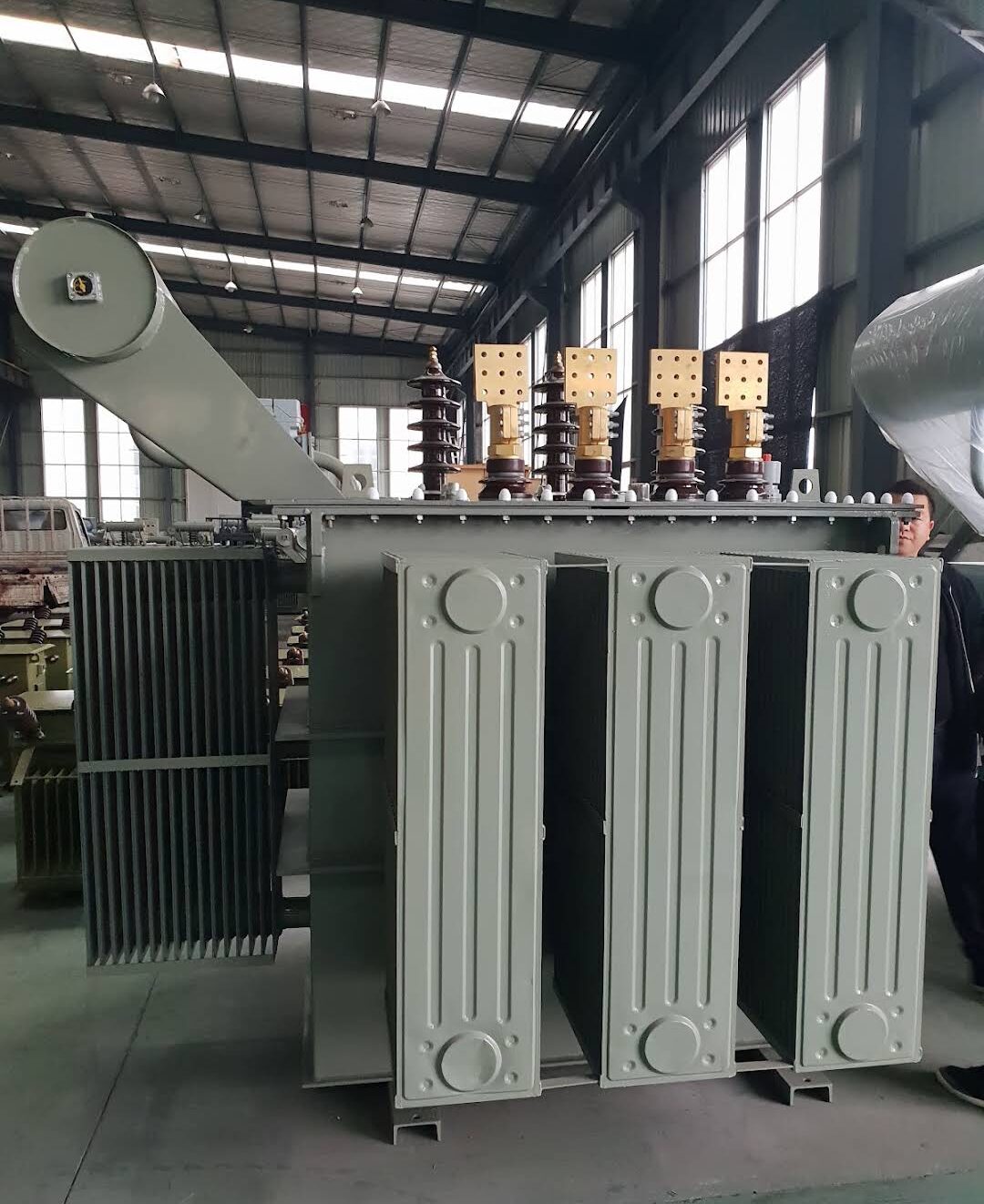 Oil-immersed transformer with radiator panels and bushings in a factory hall