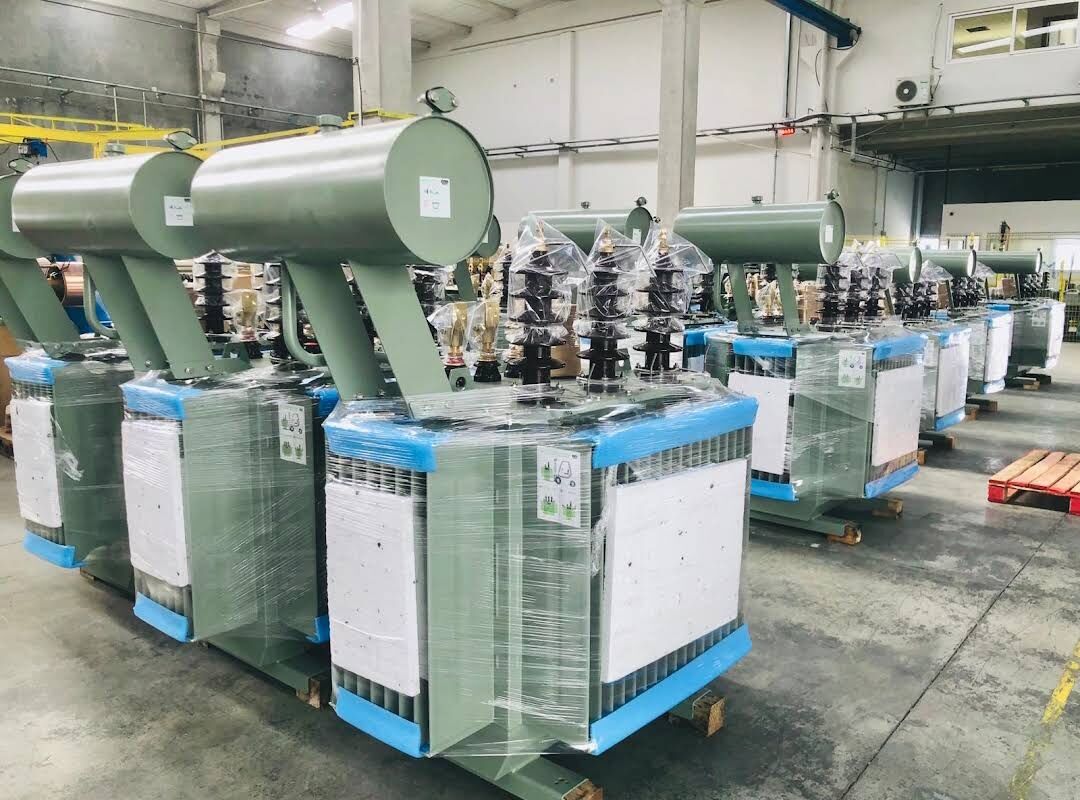 Row of wrapped transformers with conservator tanks on a factory floor