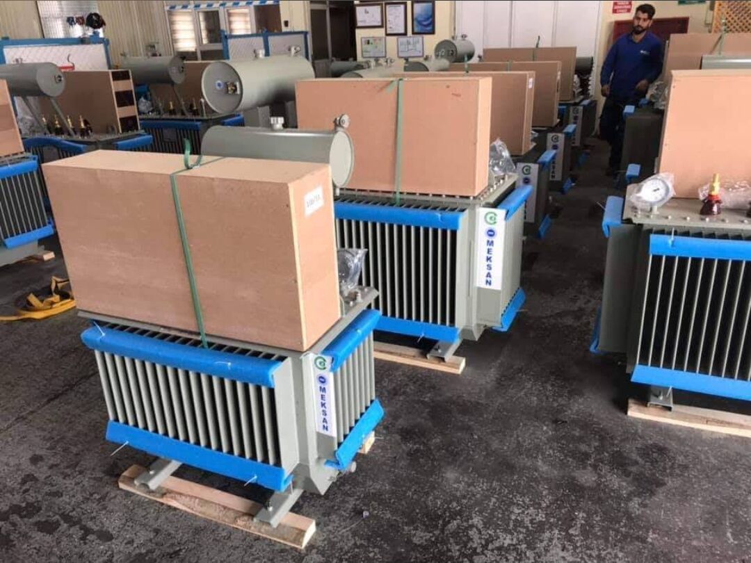 Distribution transformers with blue protective packaging lined up in a workshop
